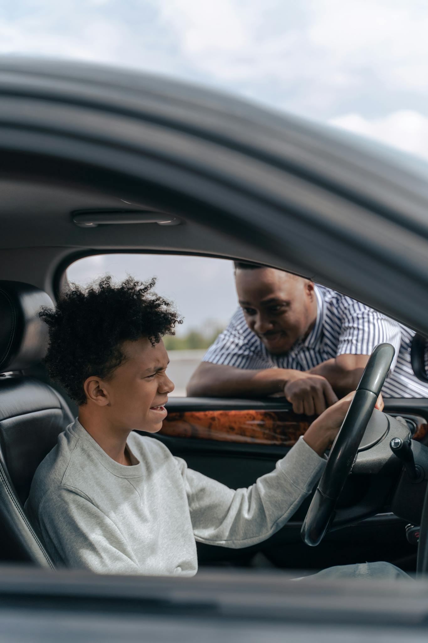 Father instructs son in car driving lesson inside a vehicle on a sunny day.